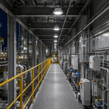 Row of 100W C1D1 round LED high bay lights delivering 13,500 lumens of 5000K illumination along a refinery corridor.
