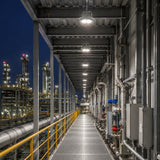 Row of 150W C1D1 round LED high bay lights delivering 21,000 lumens of 5000K illumination along a refinery walkway.