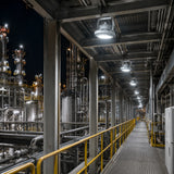 Row of 80W C1D1 round LED high bay lights delivering 10,800 lumens of 5000K illumination along a refinery walkway